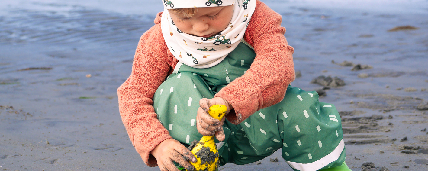 Kleinkind am Strand mit Spielsachen und Matschhose